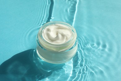 Photo of Jar with moisturizing cream in water on light blue background