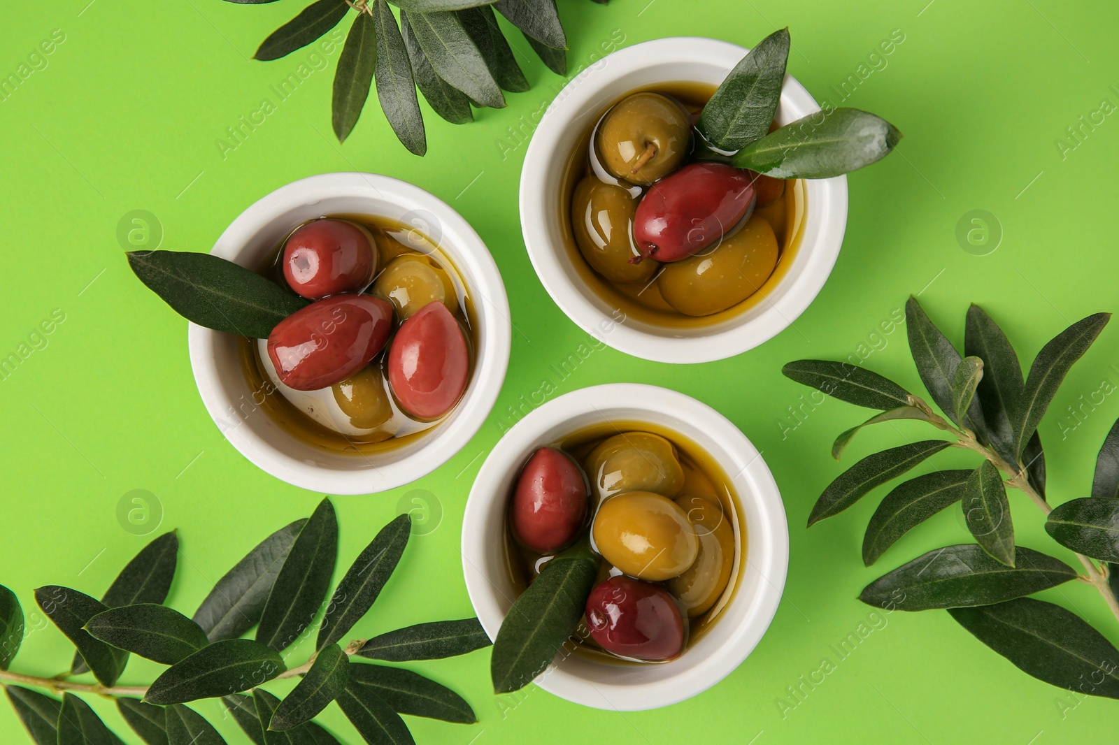 Photo of Bowls with different ripe olives and leaves on light green background, flat lay