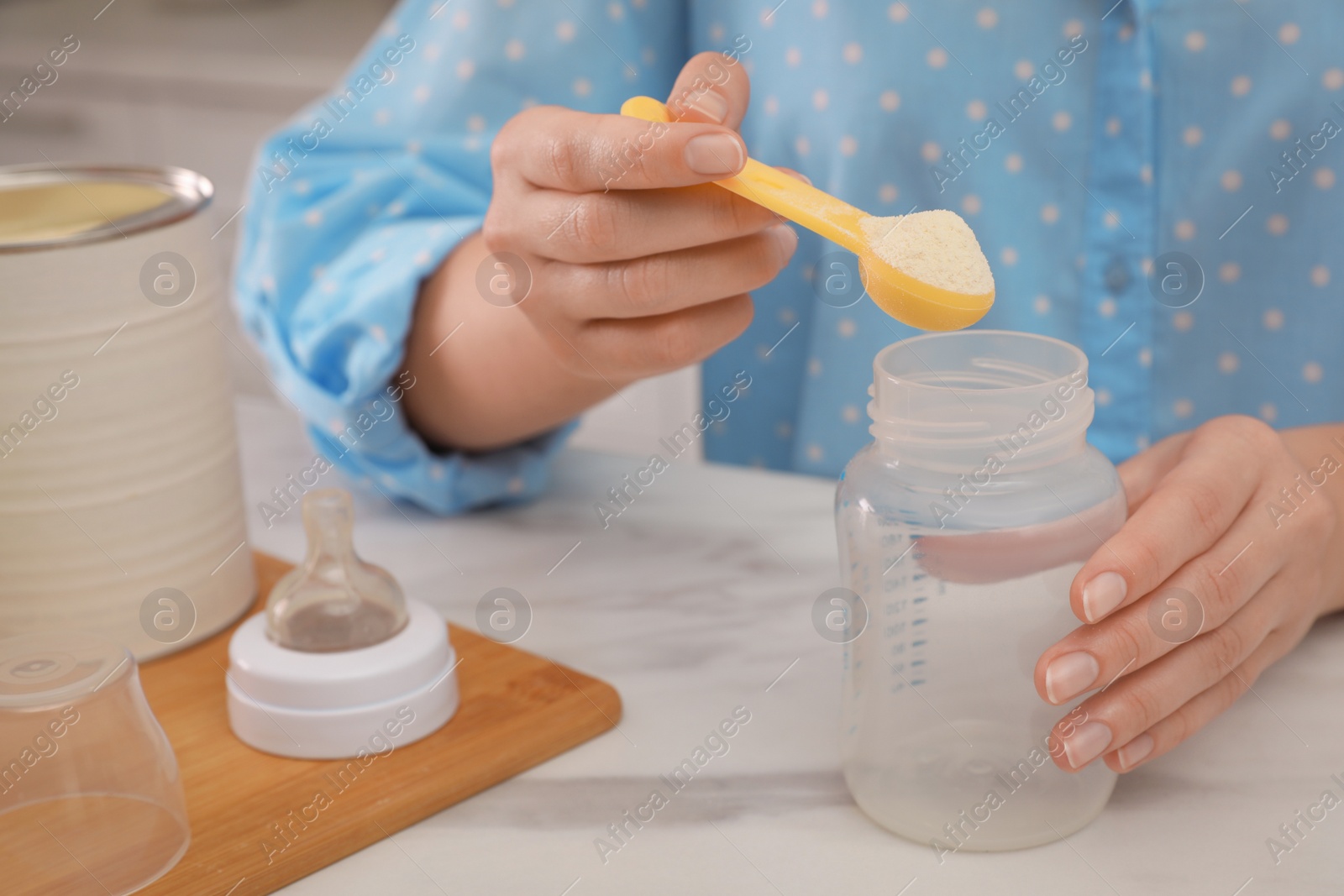 Photo of Woman preparing infant formula at table indoors, closeup. Baby milk