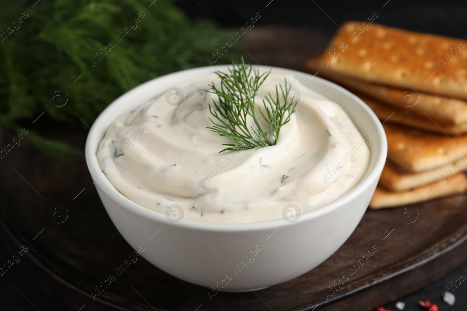 Photo of Tasty creamy dill sauce in bowl on wooden board, closeup