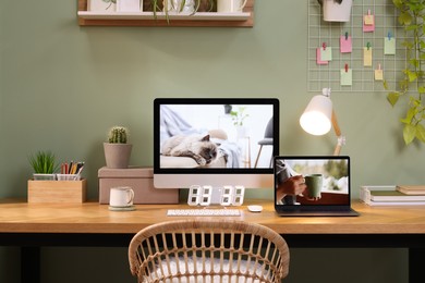 Stylish workplace with computer, laptop and lamp near olive wall at home