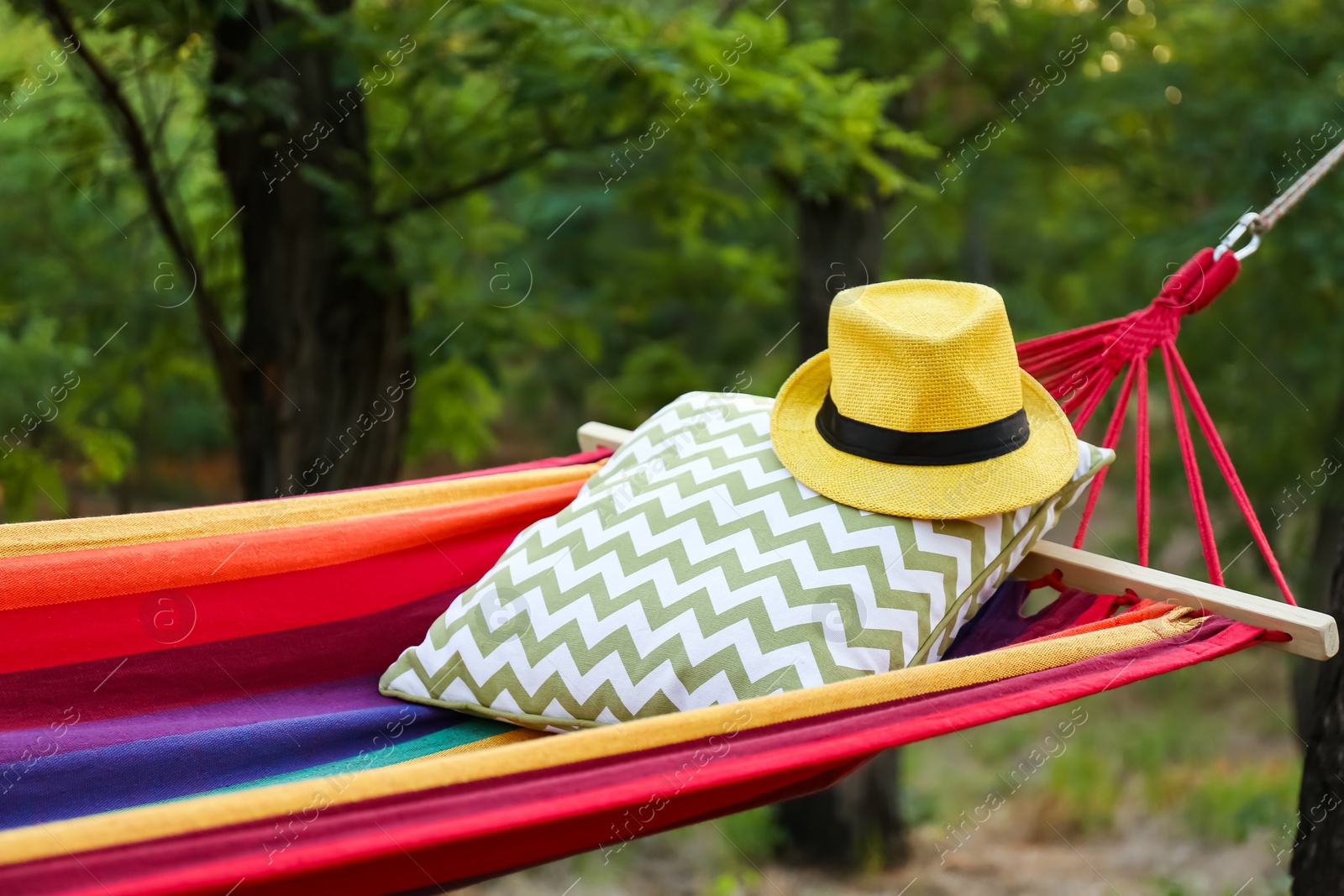 Photo of Comfortable bright hammock with soft pillow and hat at green garden, closeup