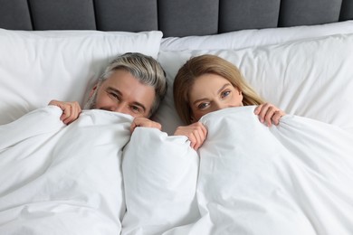 Lovely mature couple hiding together under blanket in bed at home, above view