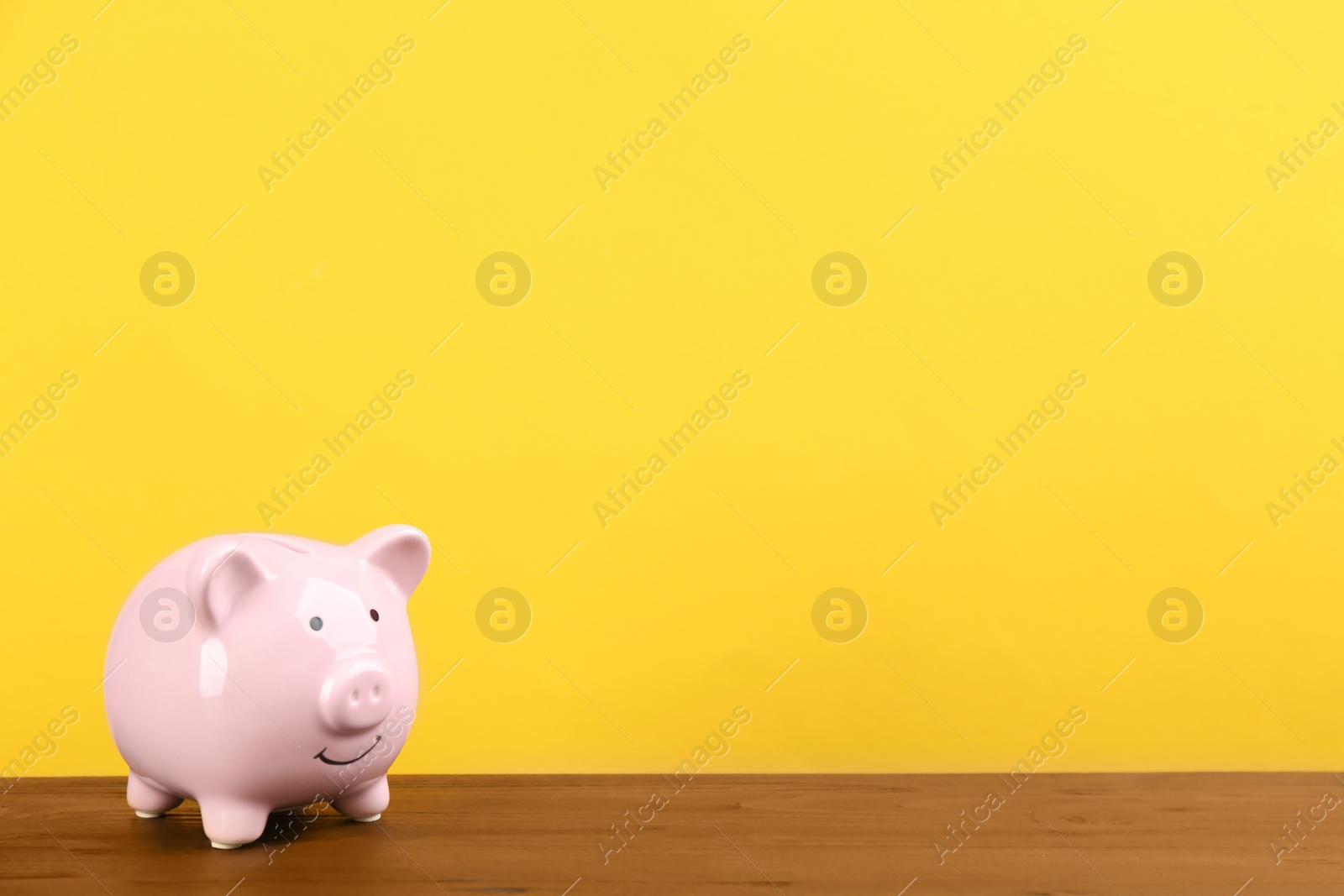 Photo of Pink piggy bank on wooden table against yellow background. Space for text