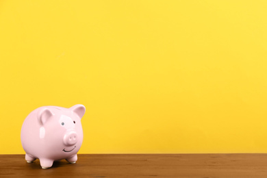 Photo of Pink piggy bank on wooden table against yellow background. Space for text