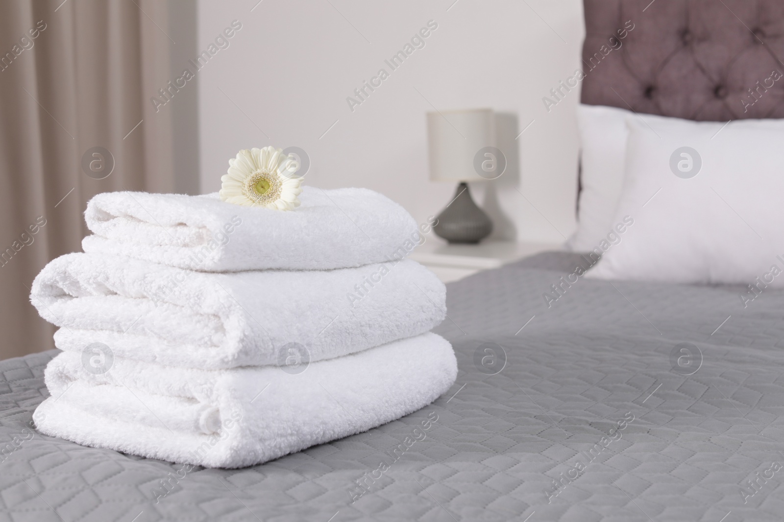 Photo of Stack of fresh towels with flower on bed in hotel room