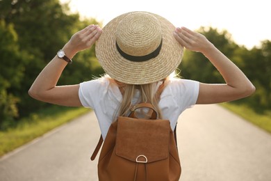 Photo of Young woman in straw hat outdoors on spring day, back view