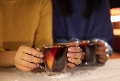 Photo of Friends with cups of mulled wine at snowy table, closeup