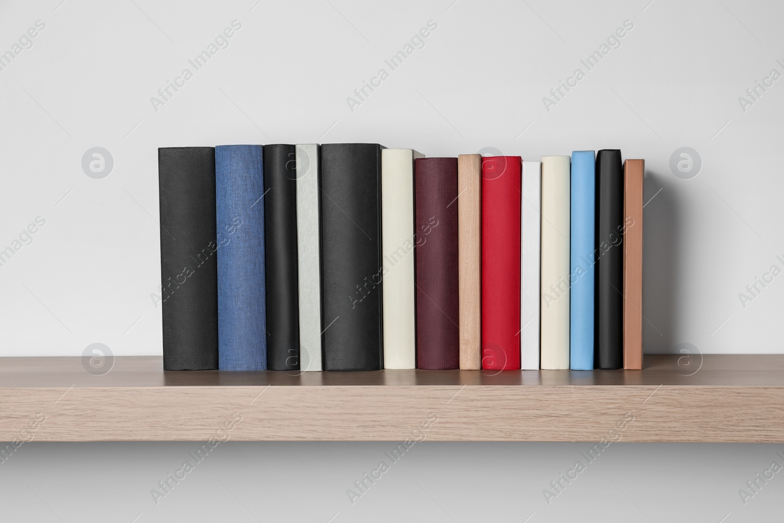 Photo of Many hardcover books on wooden shelf near white wall