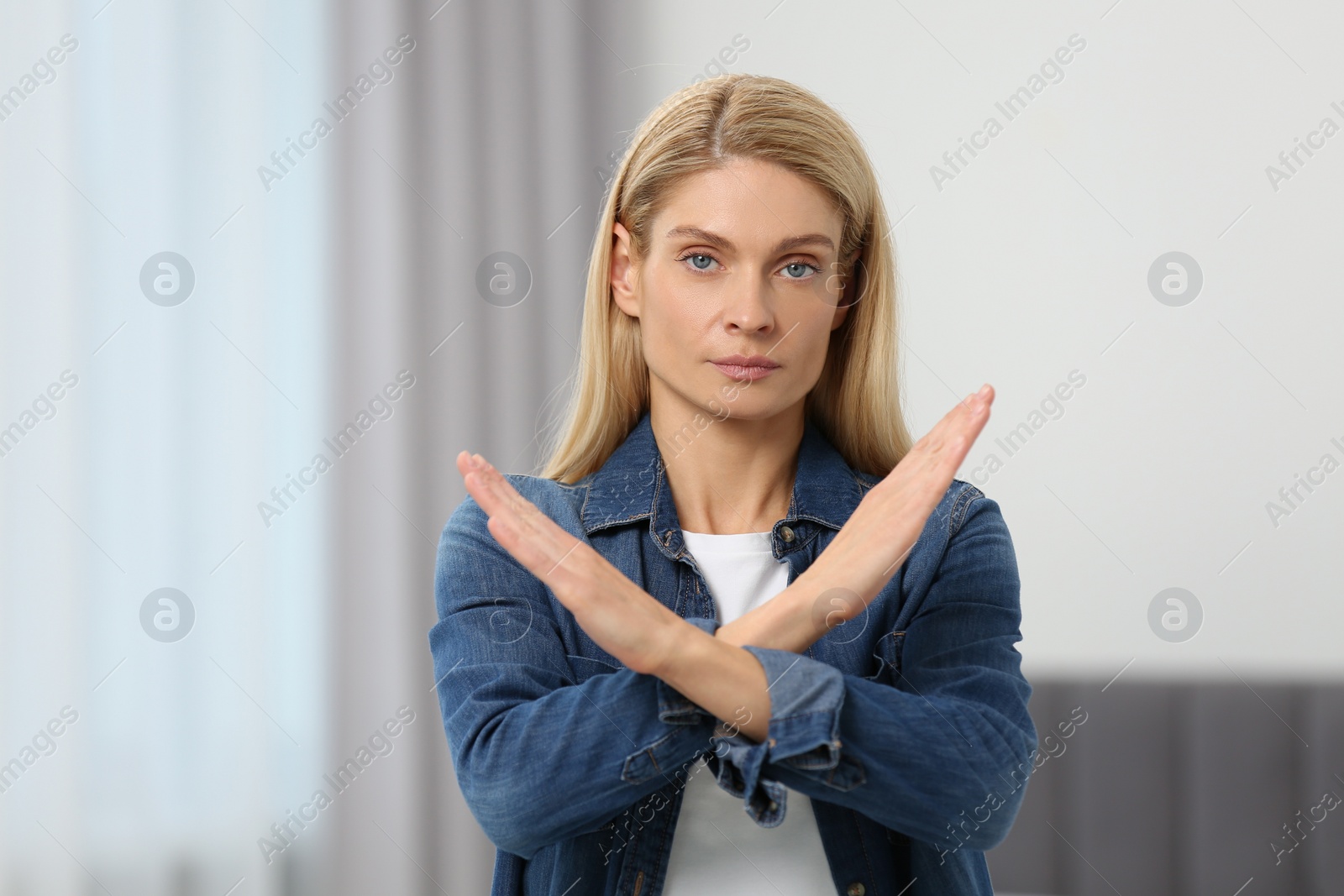 Photo of Stop gesture. Woman with crossed hands in room