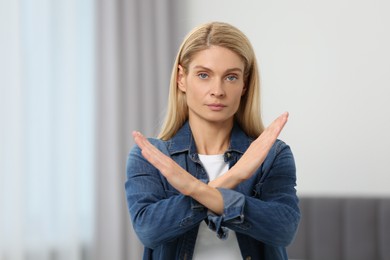 Photo of Stop gesture. Woman with crossed hands in room