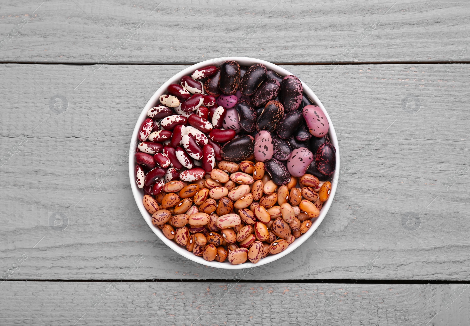 Photo of Different kinds of dry kidney beans in bowl on light grey wooden table, top view