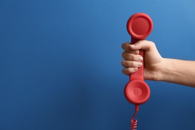 Photo of Closeup view of woman holding red corded telephone handset on blue background, space for text. Hotline concept