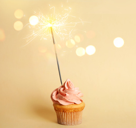 Birthday cupcake with sparkler on beige background