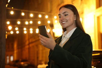 Smiling woman using smartphone on night city street. Space for text