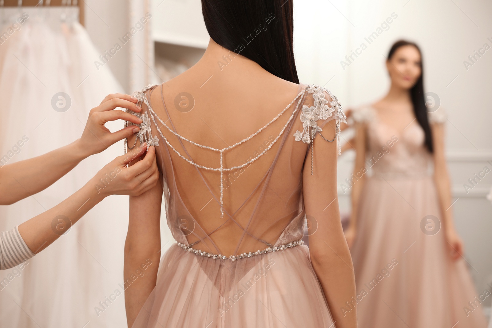 Photo of Woman trying on beautiful wedding dress in boutique, back view