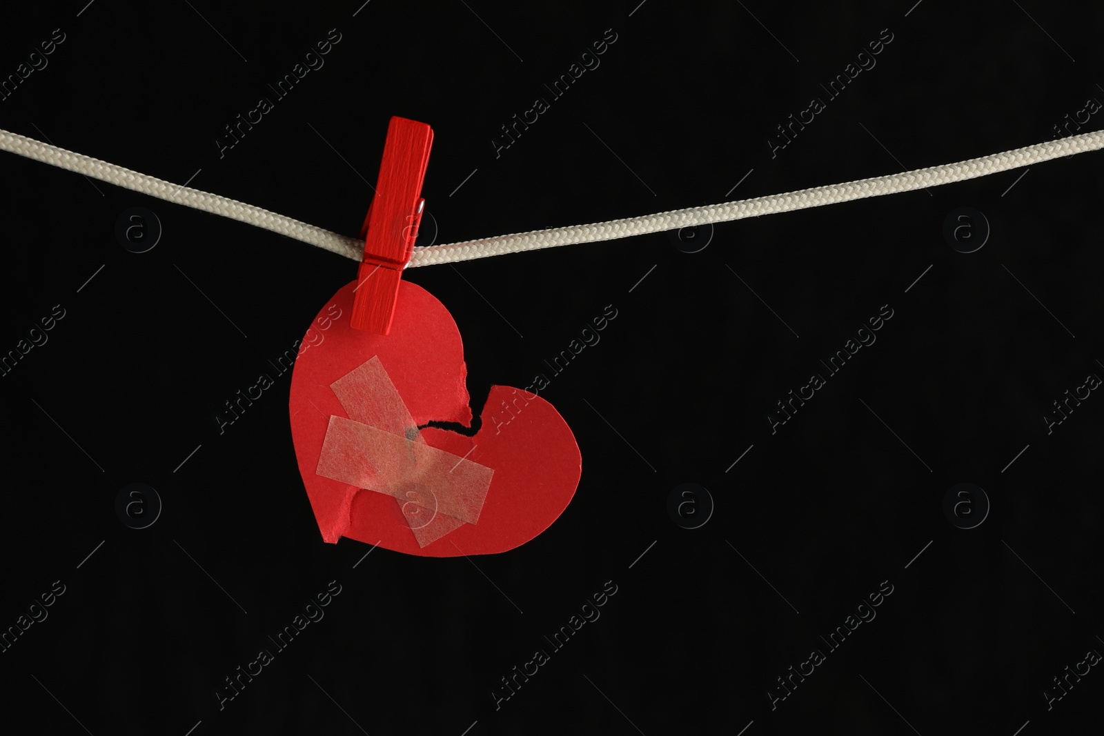 Photo of Broken heart. Torn red paper heart with medical adhesive bandages on black background, space for text