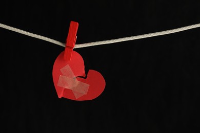 Photo of Broken heart. Torn red paper heart with medical adhesive bandages on black background, space for text