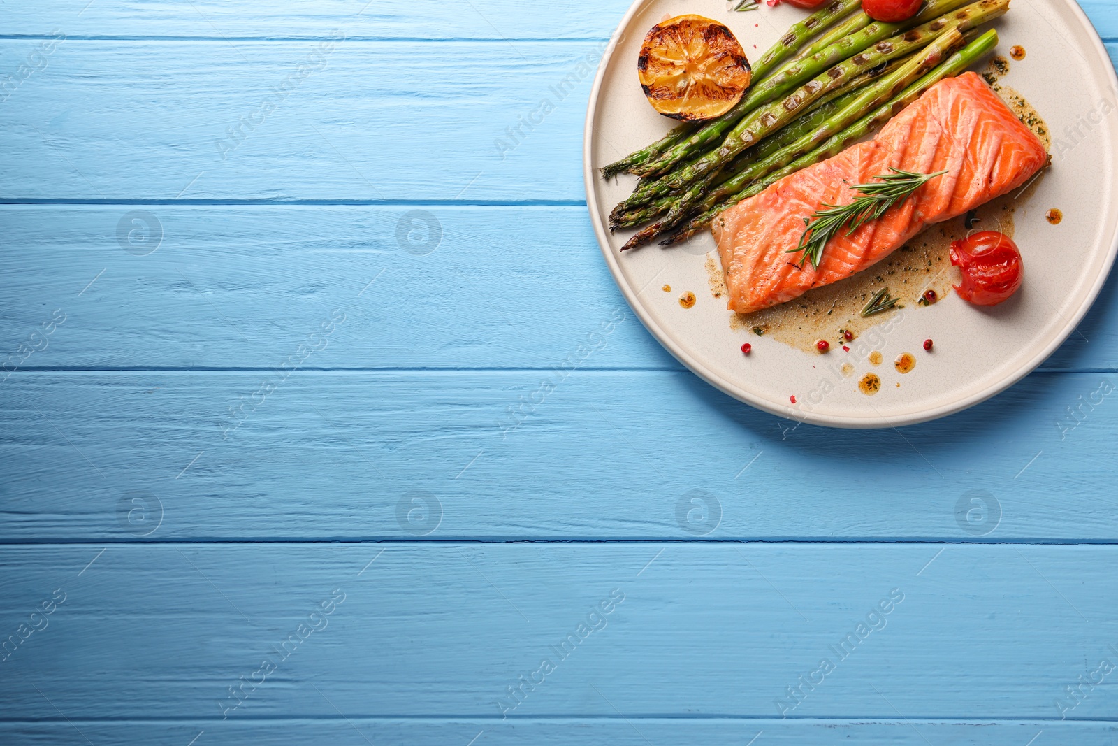 Photo of Tasty grilled salmon with asparagus, lemon and spices on light blue wooden table, top view. Space for text