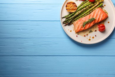 Photo of Tasty grilled salmon with asparagus, lemon and spices on light blue wooden table, top view. Space for text