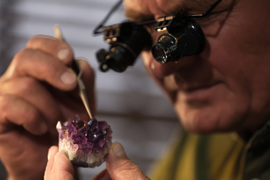 Photo of Professional jeweler working with beautiful amethyst indoors, closeup