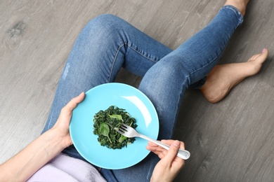 Photo of Young woman with tasty cooked spinach on wooden floor, closeup. Healthy food