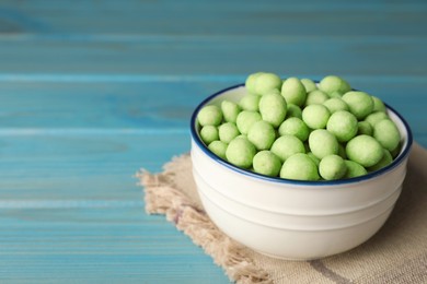 Photo of Tasty wasabi coated peanuts in bowl on turquoise wooden table, closeup. Space for text