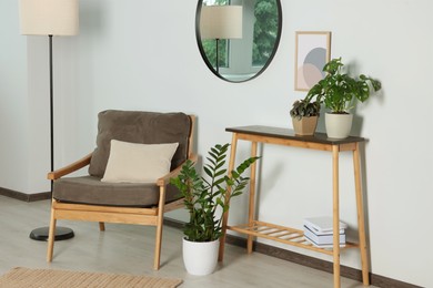 Stylish living room interior with wooden furniture, houseplants and round mirror on white wall