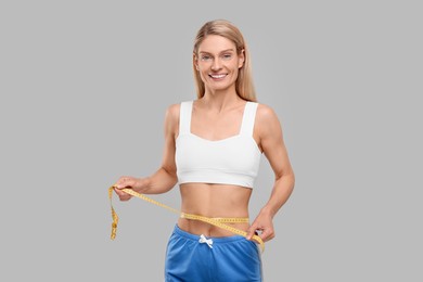 Photo of Slim woman measuring waist with tape on grey background. Weight loss