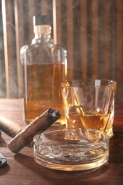Photo of Smoldering cigar, ashtray and whiskey on wooden table
