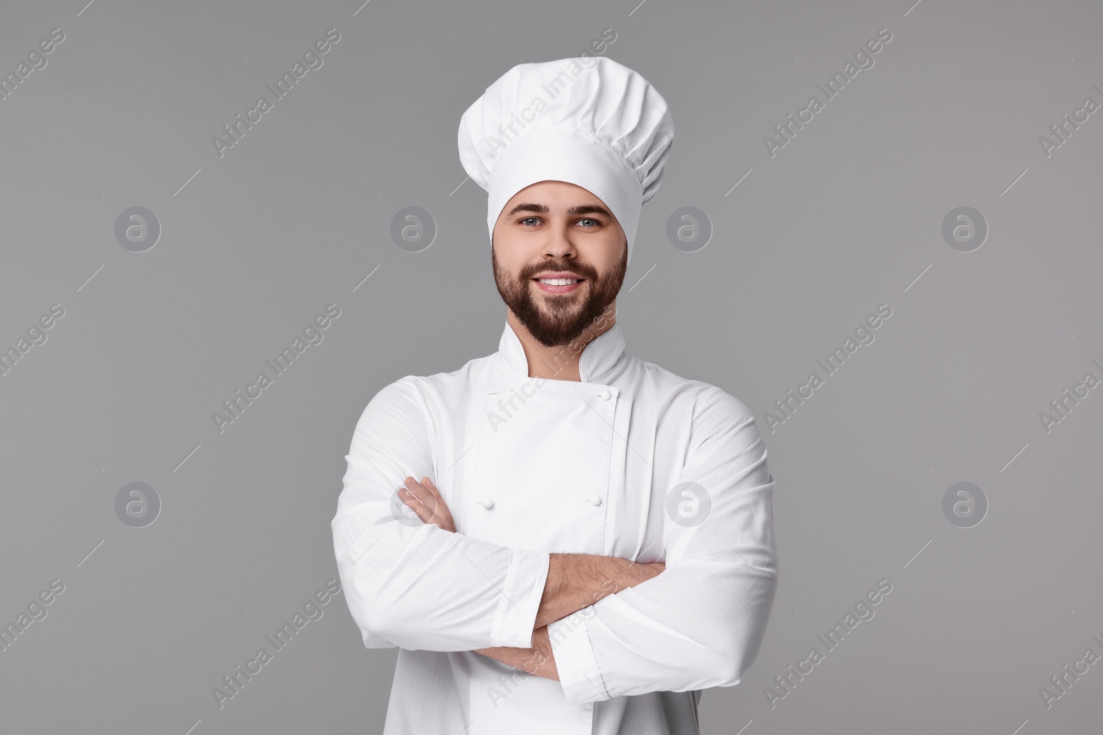 Photo of Happy young chef in uniform on grey background