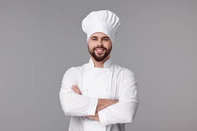 Happy young chef in uniform on grey background