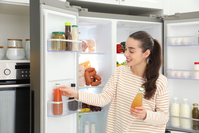 Photo of Young woman taking juice out of refrigerator in kitchen