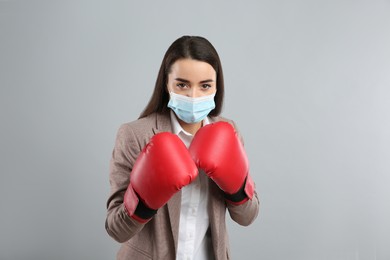 Photo of Businesswoman with protective mask and boxing gloves on light grey background. Strong immunity concept