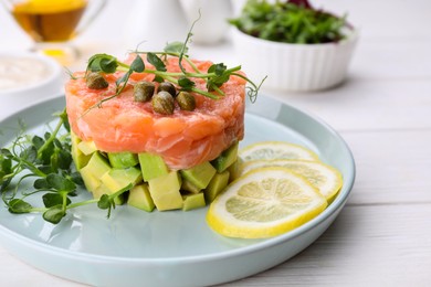 Photo of Tasty salmon tartare with avocado, lemon, capers and microgreens on white wooden table, closeup