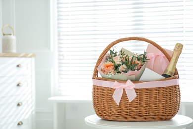 Wicker basket with gifts on table indoors. Space for text