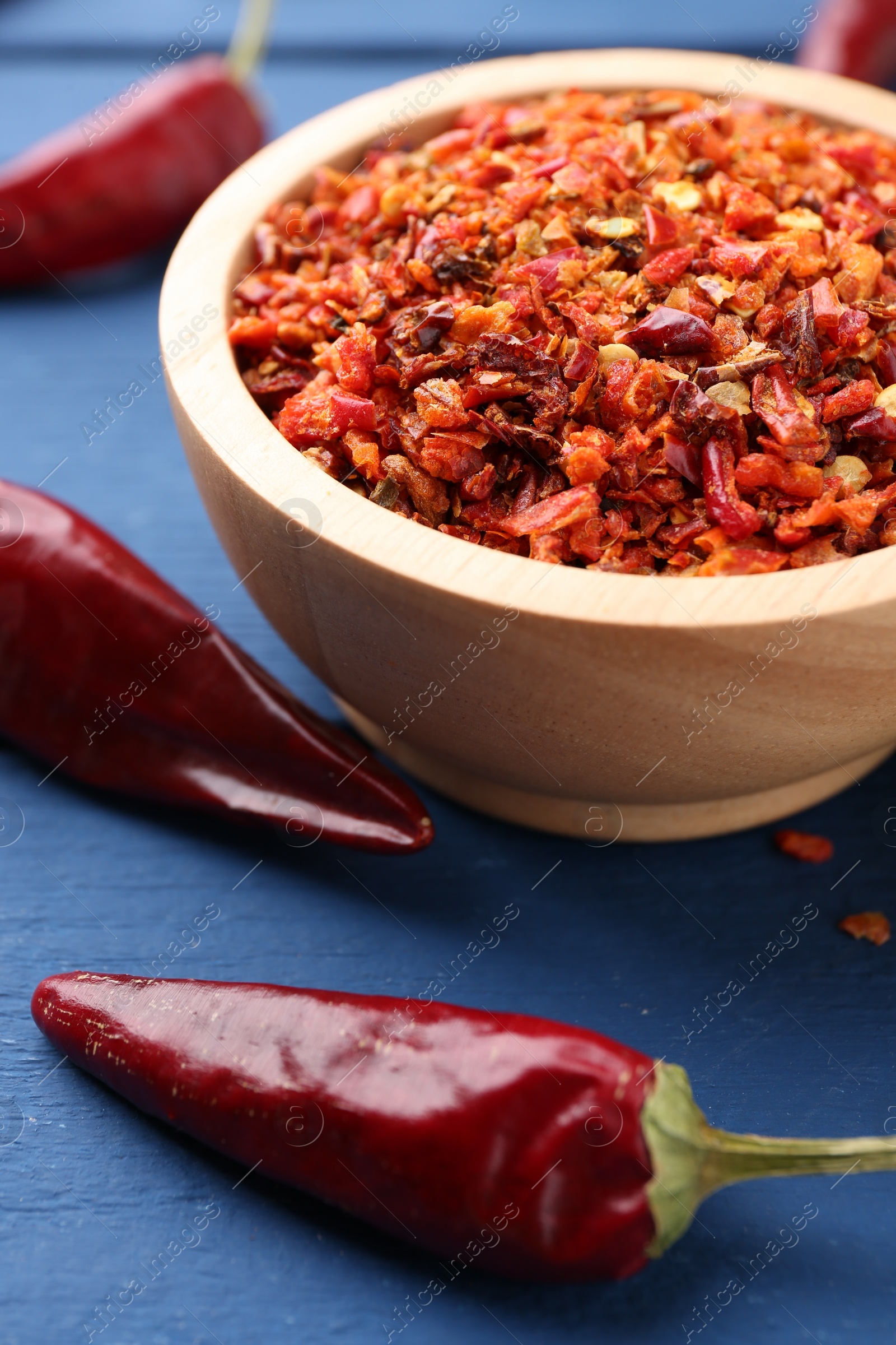 Photo of Chili pepper flakes in bowl and pods on blue wooden table, closeup