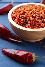 Photo of Chili pepper flakes in bowl and pods on blue wooden table, closeup