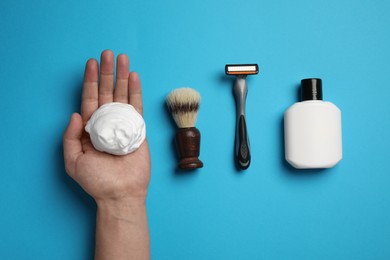 Photo of Man with shaving foam, brush, razor and bottle on light blue background, top view