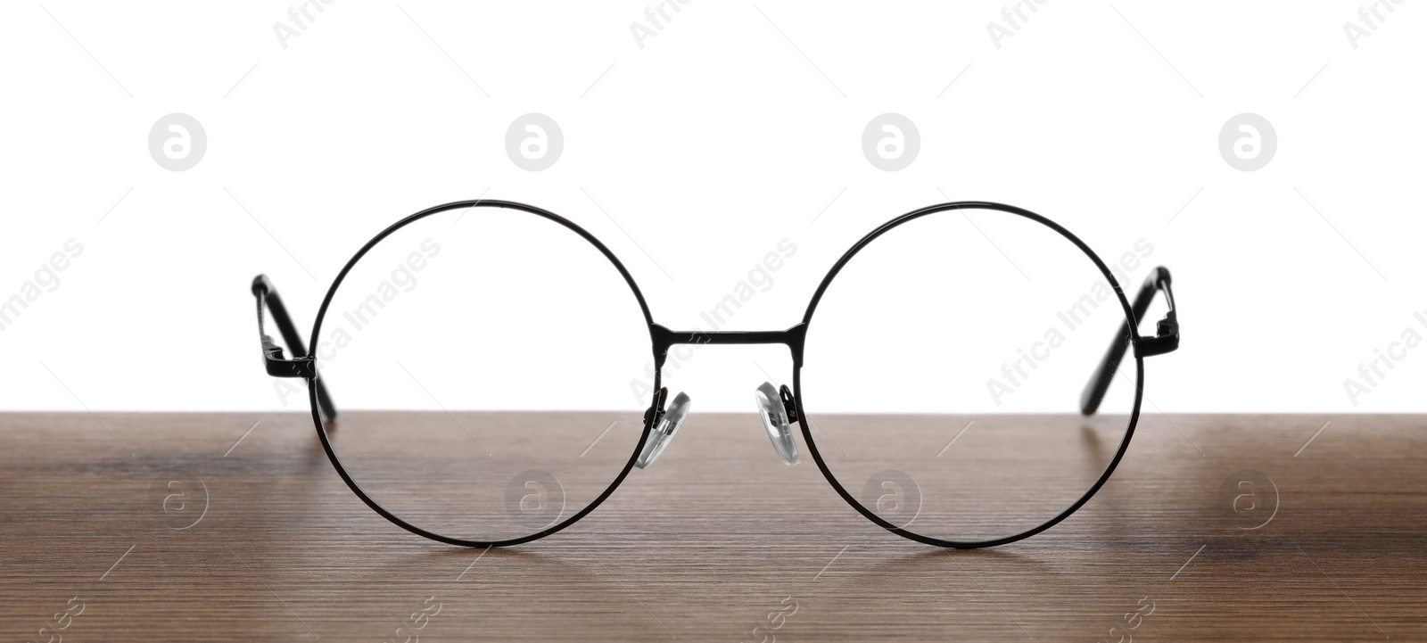 Photo of Round glasses with metal frame on wooden table against white background
