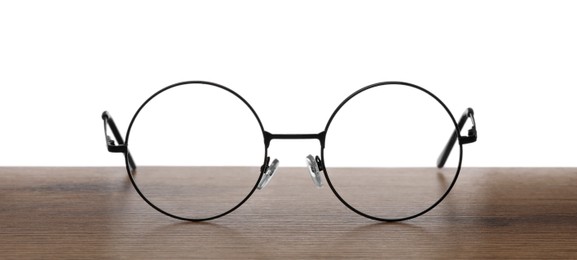 Round glasses with metal frame on wooden table against white background