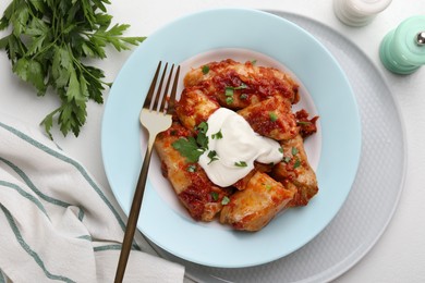 Photo of Delicious stuffed cabbage rolls served with sour cream on white table, flat lay