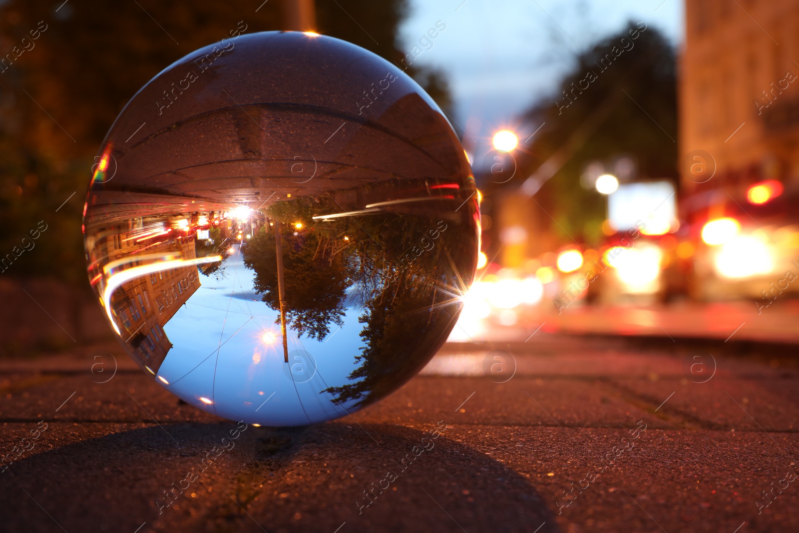 Photo of Beautiful city street, overturned reflection. Crystal ball on asphalt road at night, closeup. Space for text