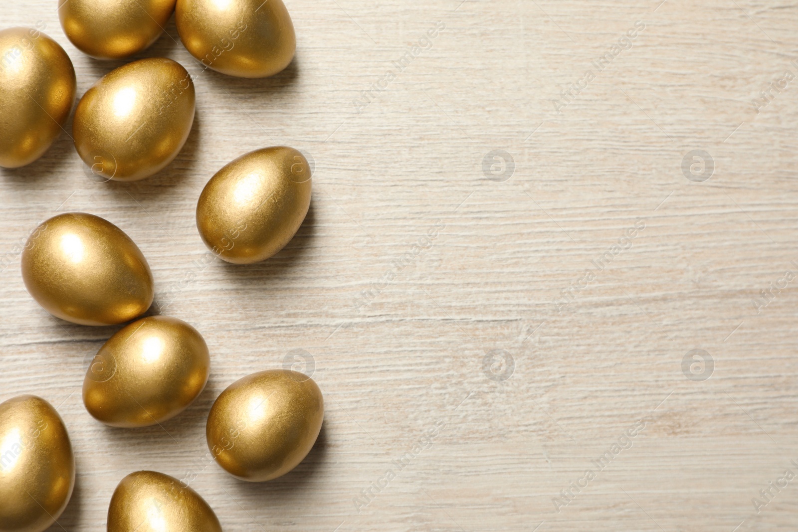 Photo of Many golden eggs on white wooden table, flat lay. Space for text