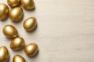 Photo of Many golden eggs on white wooden table, flat lay. Space for text