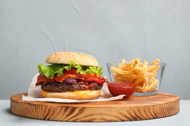 Photo of Board with tasty burger and french fries on table against grey background