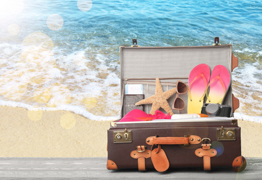 Image of Suitcase with different beach objects on grey wooden table near sea. Space for text