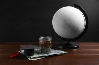 Photo of Scholarship concept. Graduation cap, money and globe on wooden table