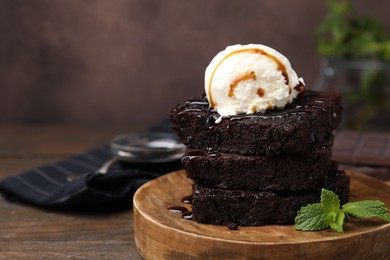 Delicious brownies served with ice cream and caramel sauce on wooden table, closeup. Space for text