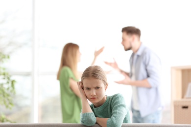 Little unhappy girl sitting on sofa while parents arguing at home